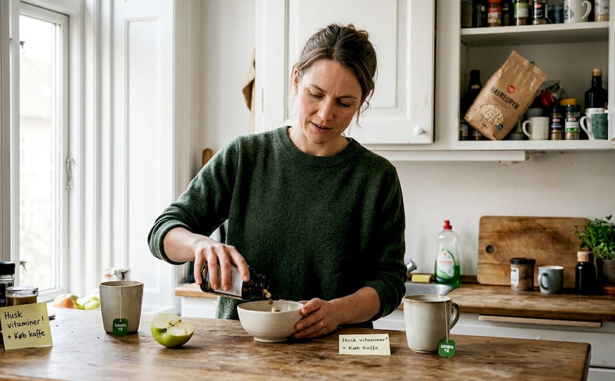 En kvinde står hjemme i sit køkken og doserer vitaminer.