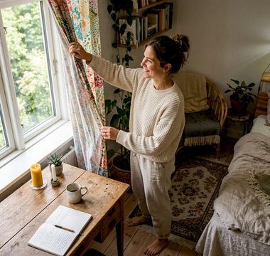 En kvinde trækker gardinerne fra og lader morgensolen strømme ind i soveværelset.