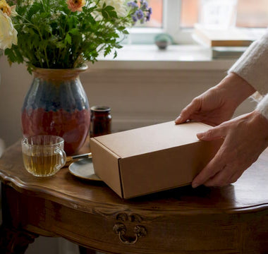 Et par hænder sætter en pakke vitaminer op på en træhylde.