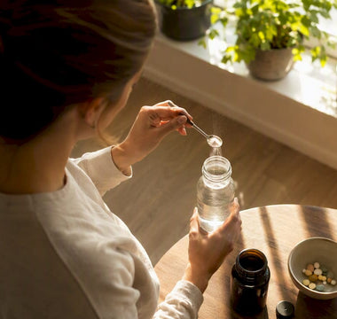 Et par hænder hælder magnesiumpulver op i et glas, mens der ligger vitamin D-kapsler ved siden af.
